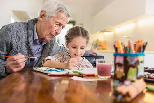 Girl and grandfather painting at kitchen table