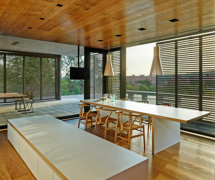 PX House, La Garriga, Spain. Spacious dining area with long white table and chairs. White bench and floor to ceiling windows.