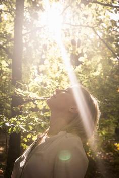 Mature woman standing in stream of light in forest
