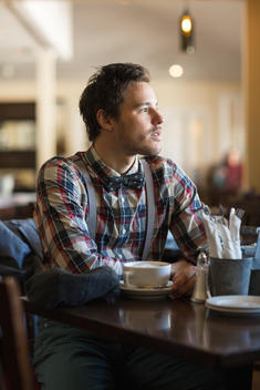 20 something man in checkered shirt sitting on table at cafe.