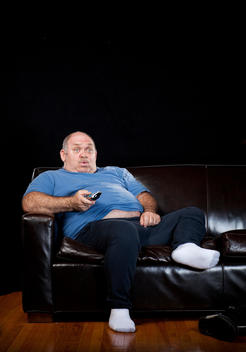 A fat middle-aged man relaxes on a couch with a remote in his hand