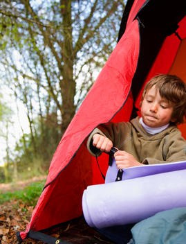 Portrait of a boy sitting in a tent rolling a sleeping mat