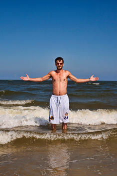 Portrait Of A Man Wearing Sunglasses With Arms Out Stretched At The Beach.