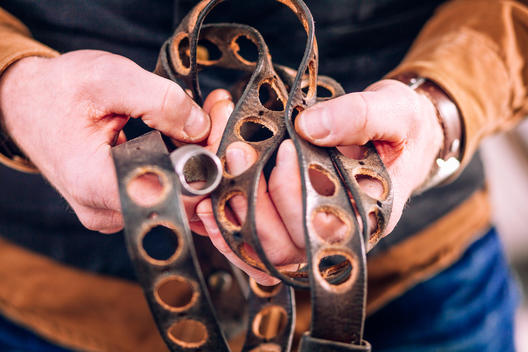 Midsection of worker holding leather belts with holes in factory