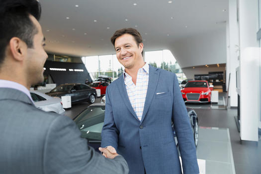 Salesman and man handshaking in car dealership showroom
