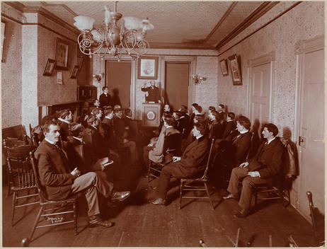 Group Of Seated Young Men, Listening To A Speaker At A Podium.