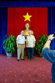 two older men having their picture taken standing in front of a Ho Chi Min Statue at the Presidential Palace in Saigon
