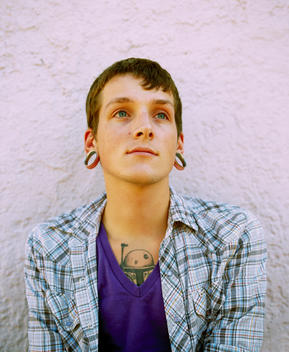 Natural light pure Portrait of a young man with tattoos and gauged ears.