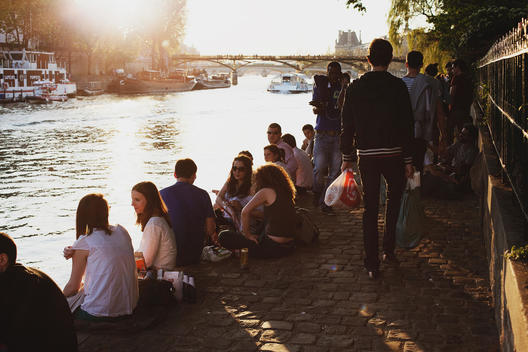 A group of young people sitting along the Seine river at sunset in Paris.