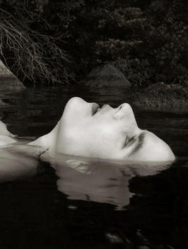 Close up of a female face calmly looking up partially submerged in an outdoor lake