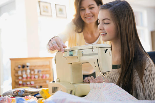 Mother teaching daughter how to use sewing machine