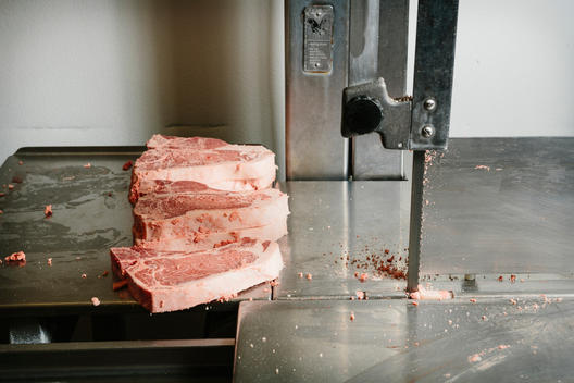 Freshly cut frozen steaks on a metal band saw table.