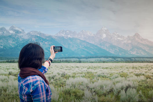 Girl using a Smartphone to take a picture of the Grand Tetons, WY.