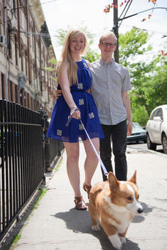 Young couple taking corgi dog for a walk along street