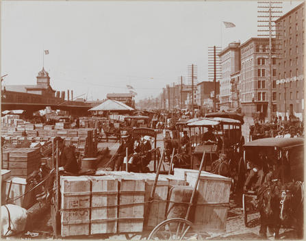 An Open-Air Marketplace Near The Water Many Horse-Drawn Carriages And Crates Of Goods Are Visible.