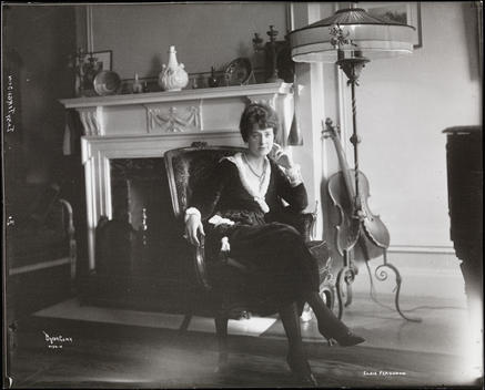 Elsie Ferguson In What Appears To Be Her Residence At 350 Park Avenue, Seated In A Chair In Front Of A Fireplace With A Cello Behind Her.