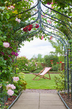 A garden with a rose arch, and a deck chair