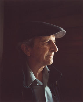 a portrait of an older man in profile smiling, wearing a cap