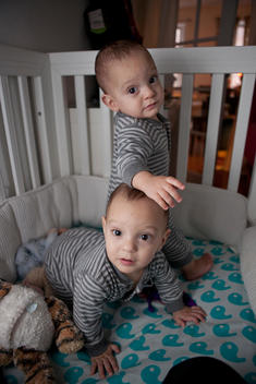 Identical twin boys in a crib, one leaning on the other