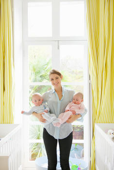 Smiling Mother Holding Twin Babies in Nursery