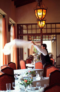 A waiter throws a tablecloth over a dining table at a Country Club\'s restaurant
