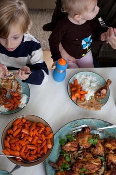 Overhead Shot Of Two Children Sitting At The Table Eating Indian Food (Chicken Masala)