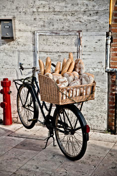 A parked bike with a basket of baguettes attached to the back.