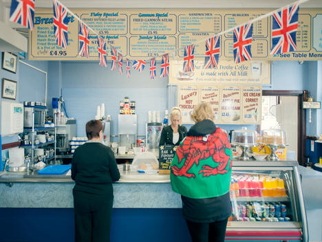 Woman draped in a Welsh flag at the counter of a traditional English Caf_ decorated with Union Flags