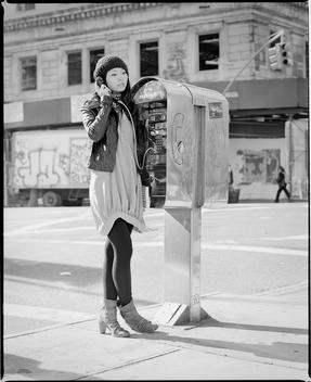A Young Asian Chinese-American Woman Makes A Phone Call On A Public Telephone On The Street Corner On Broadway Near Union Square. Models On The Street Near Union Square During A Fashion Shoot For New York City Clothing Brand Callalilai. New York, Ny
