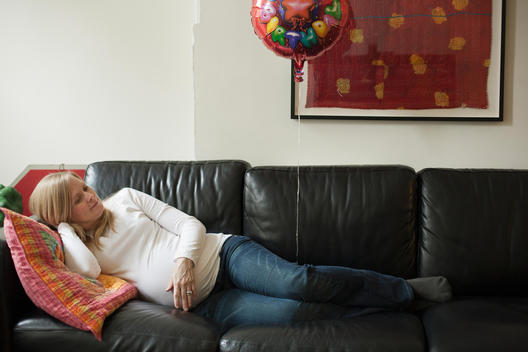 Pregnant Woman Laying On Couch With A Happy Birthday Balloon