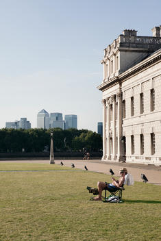 Man In Lounge Chair On University Campus With Canary Wharf In Background