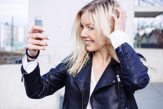 City life portrait of young woman checking her makeup and hair in Smartphone