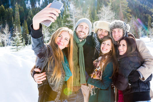 Group of 20 something year old friends taking a group selfie on snow packed road on brisk wintery day