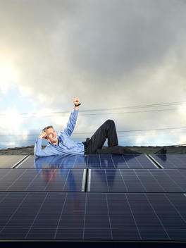 Founder of SolarCity, Lyndon Rive, lays on top of a roof covered in solar panels with one hand under his head and the other outstretched above him