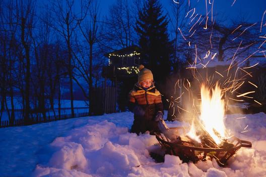 Young boy sitting by fire in snowy landscape
