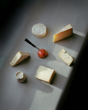 Collection of English cheeses and a knife stabbed in an apple in the center. On a grey surcease with rays of sunlight.