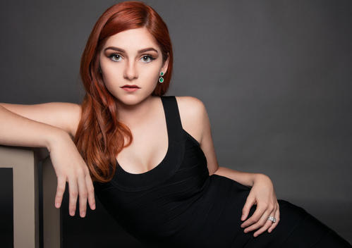 Beauty fashion portrait with a luxury aesthetic of a woman with red hair wearing emeralds and diamonds and a black dress.