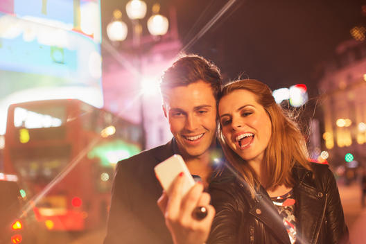 Couple taking cell phone picture together on city street at night