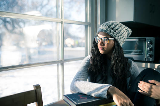 A young African-America college girl stares out a window instead of studying.
