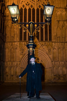 A guide doing one of the haunted tours in York stands under a lamp post in front of York Cathedral.