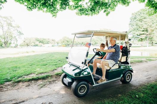 Caucasian grandfather and grandson driving golf cart on course