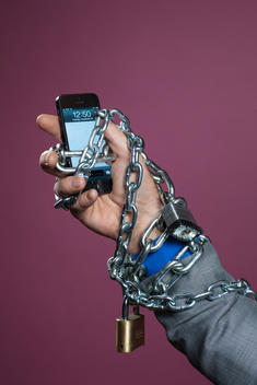 A man\'s hand holding an iPhone has chains and locks wrapped around it