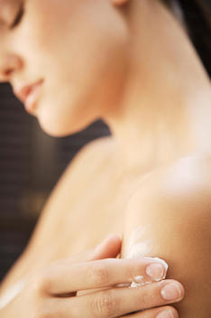 Young woman applying body lotion on shoulder