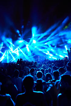 A wide shot of a concert with a DJ and light show on stage.