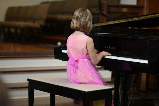 Cute caucasian girl from music class, age 6-9, practices piano before her first recital performance