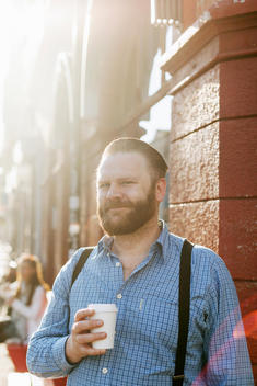 Portrait of smiling businessman holing disposable coffee cup on sidewalk