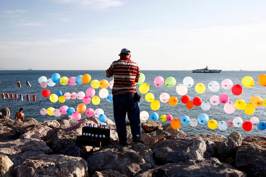 Man Standing In Front Of Rows Of Balloons Overlooking The Sea, Istanbul, Turkey.