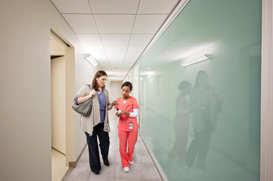 African American female nurse and white female patient, havinga conversation in a hospital hallway.