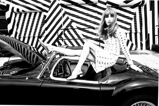 Black convertible car parked in front of a zebra like wall a model sits on the top waiting for a mechanic.