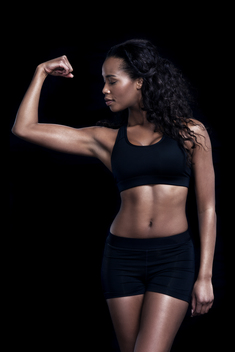 An African-American fitness model works out on a black background wearing all black clothing.